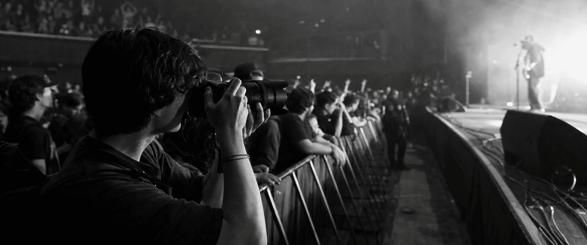 A concert photographer works from beside a stage in a black-and-white photograph.