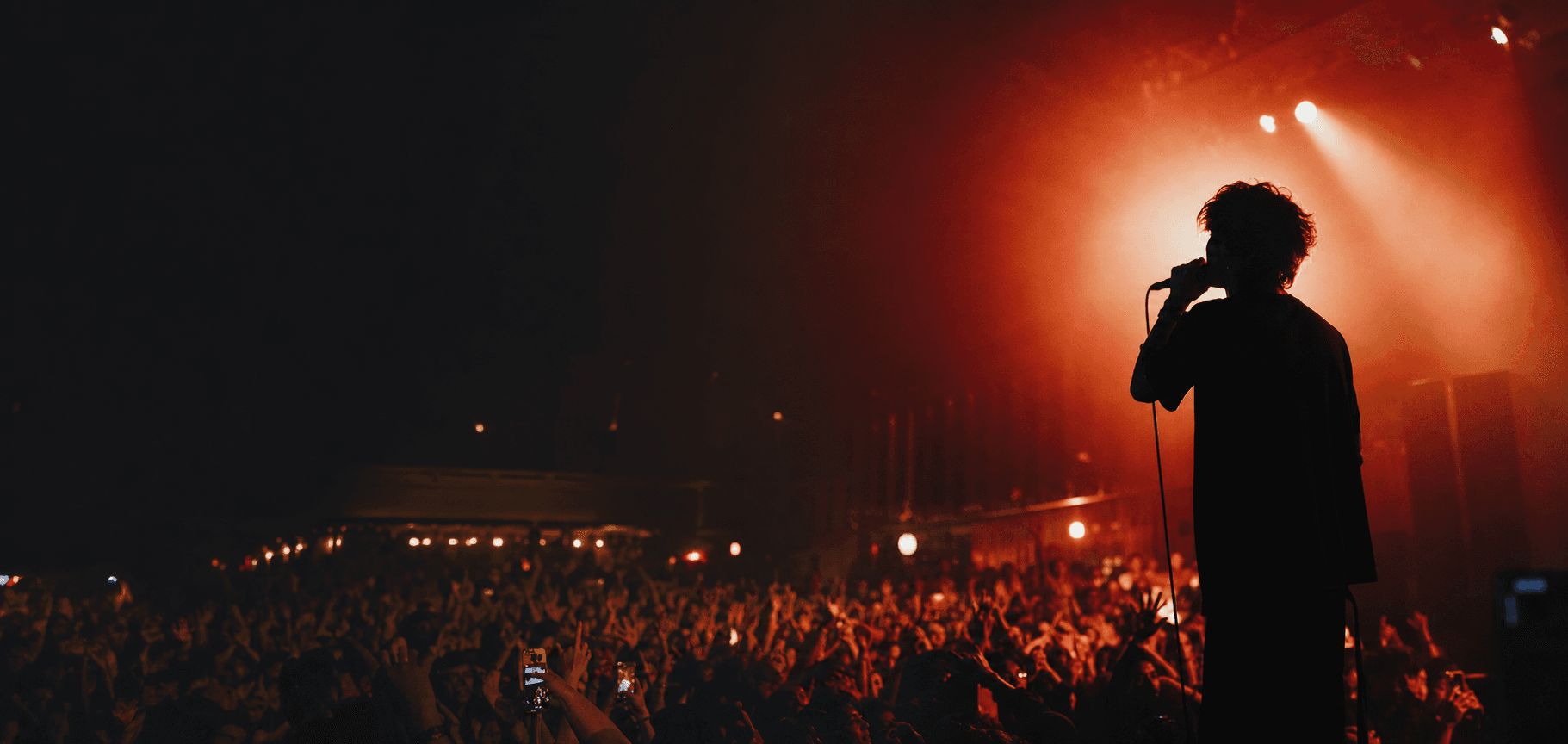 A singer silhouetted against red stage light above a crowded concert floor.